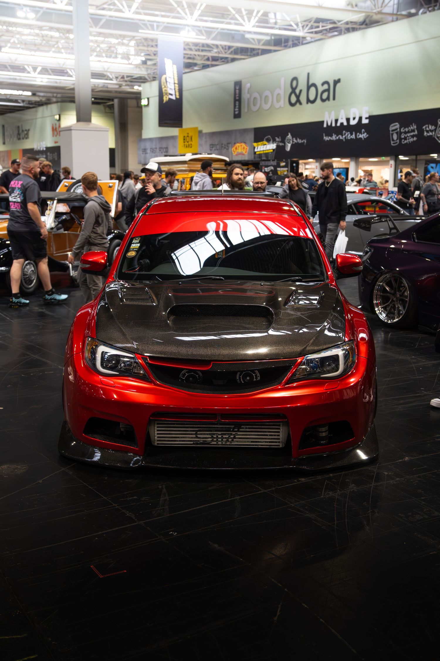 Red modified Subaru Impreza WRX STI with carbon fiber hood on display at auto show.