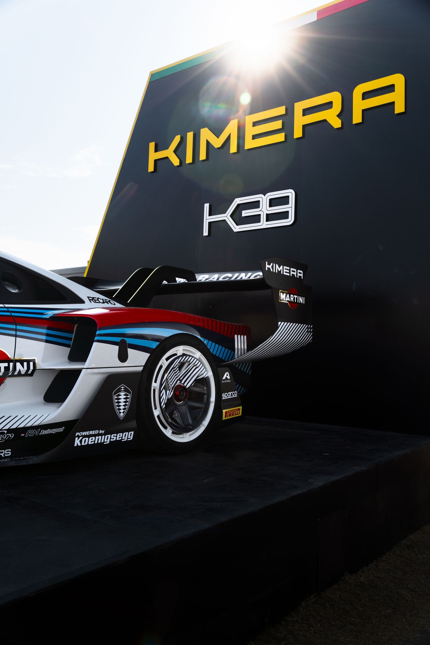 Kimera KE39 racing car with Martini livery on display, powered by Koenigsegg, under bright sunlight at a motorsport event.