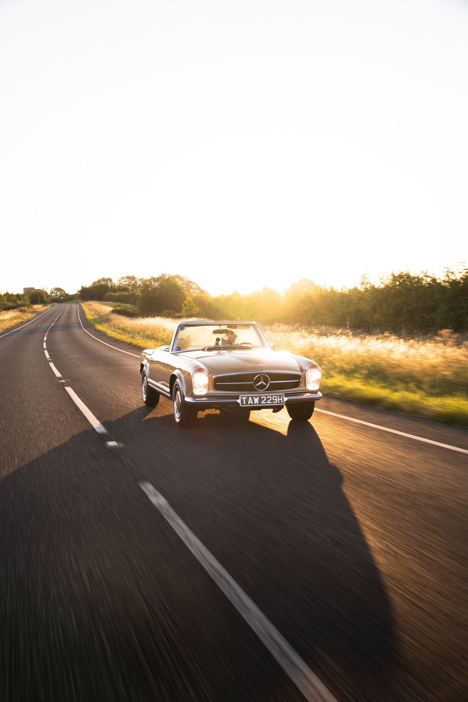 Classic Mercedes-Benz convertible driving on a scenic road at golden sunset hour.