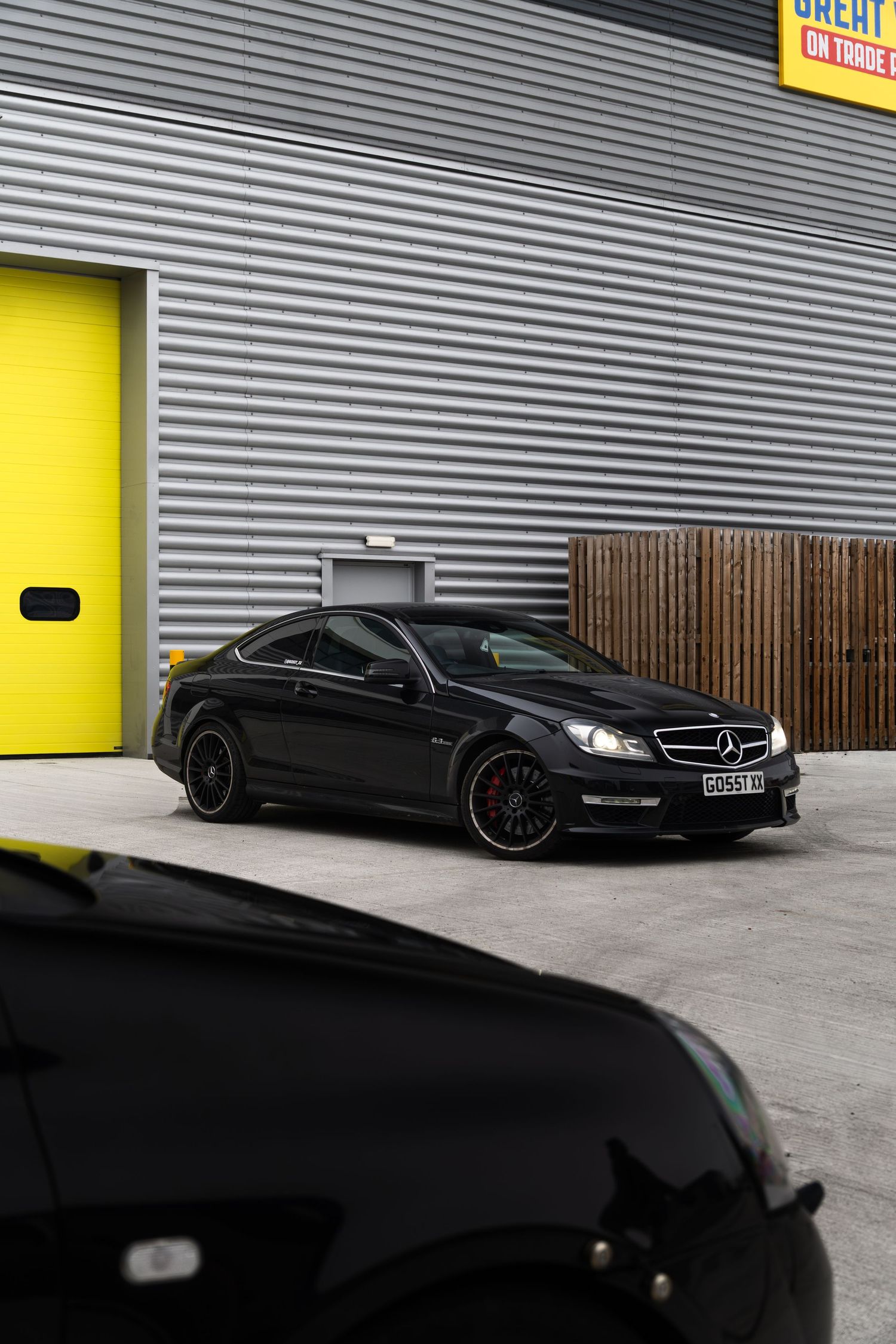 Black Mercedes-AMG C63 coupe parked in front of a corrugated metal building with yellow garage doors.