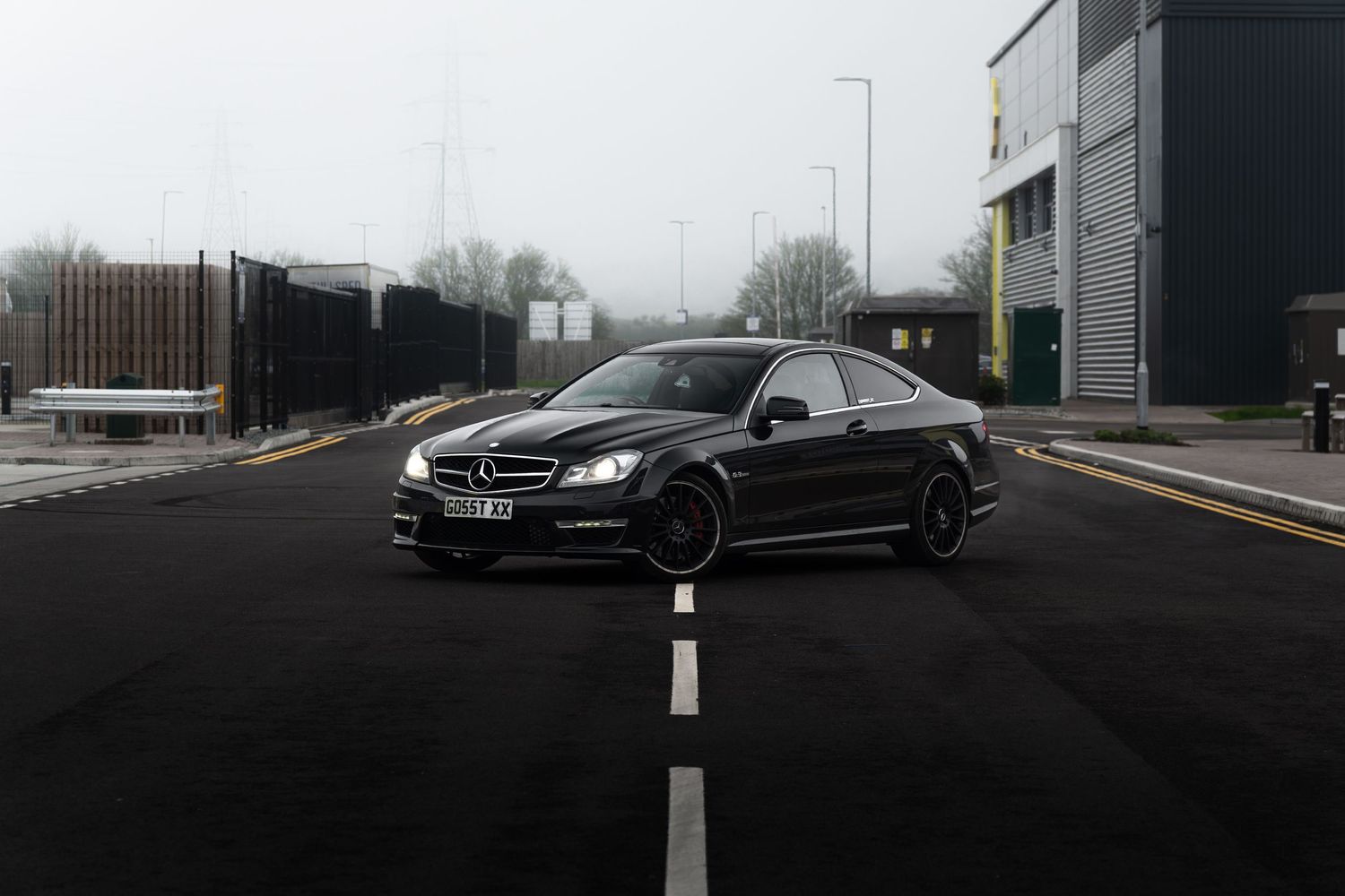 Black Mercedes-Benz C63 AMG coupe on dark wet road in foggy conditions.
