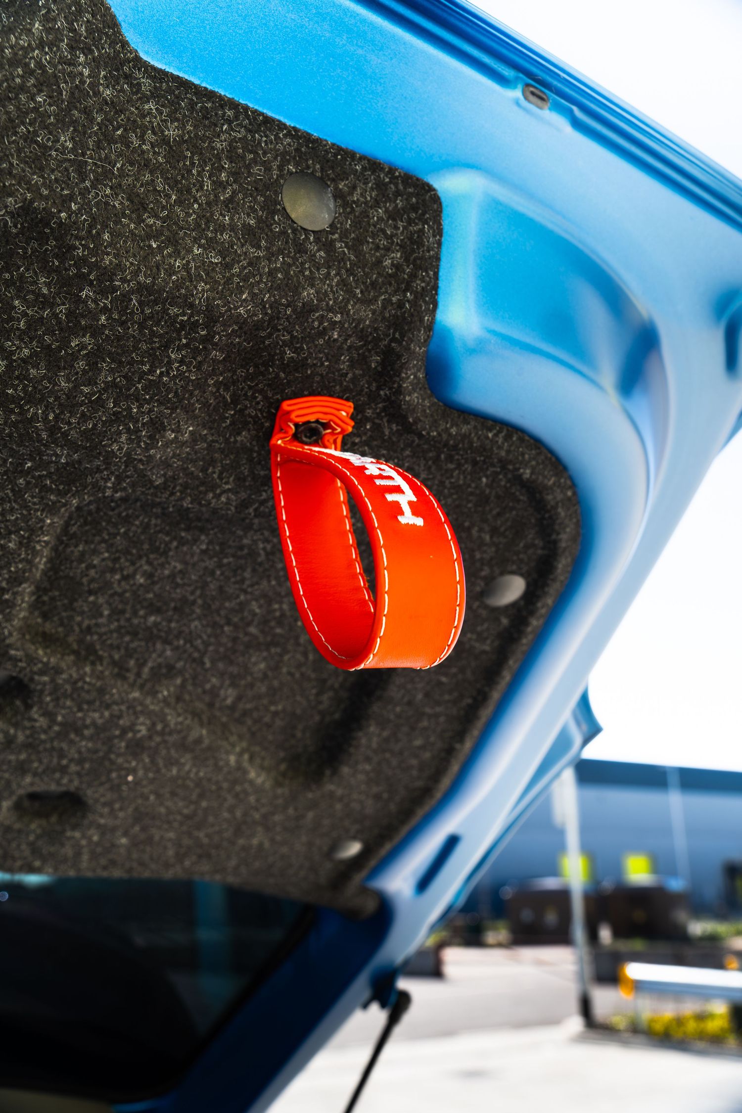 Blue Abarth boot lid interior showing an orange branded Abarth pull strap handle against grey carpet lining.