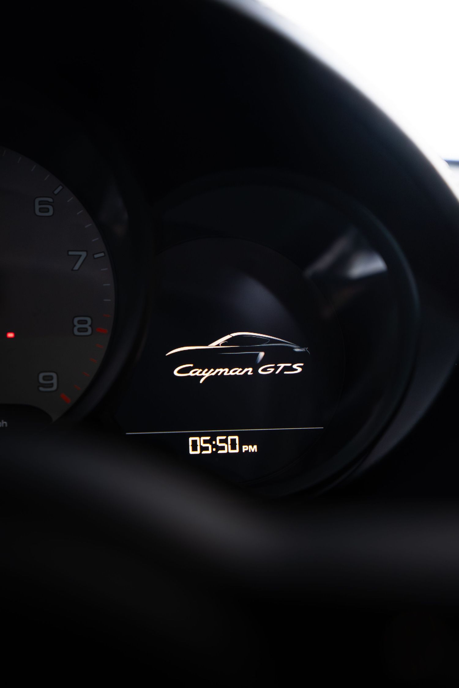 Porsche Cayman GTS digital instrument display showing model logo and 05:50 PM time readout.