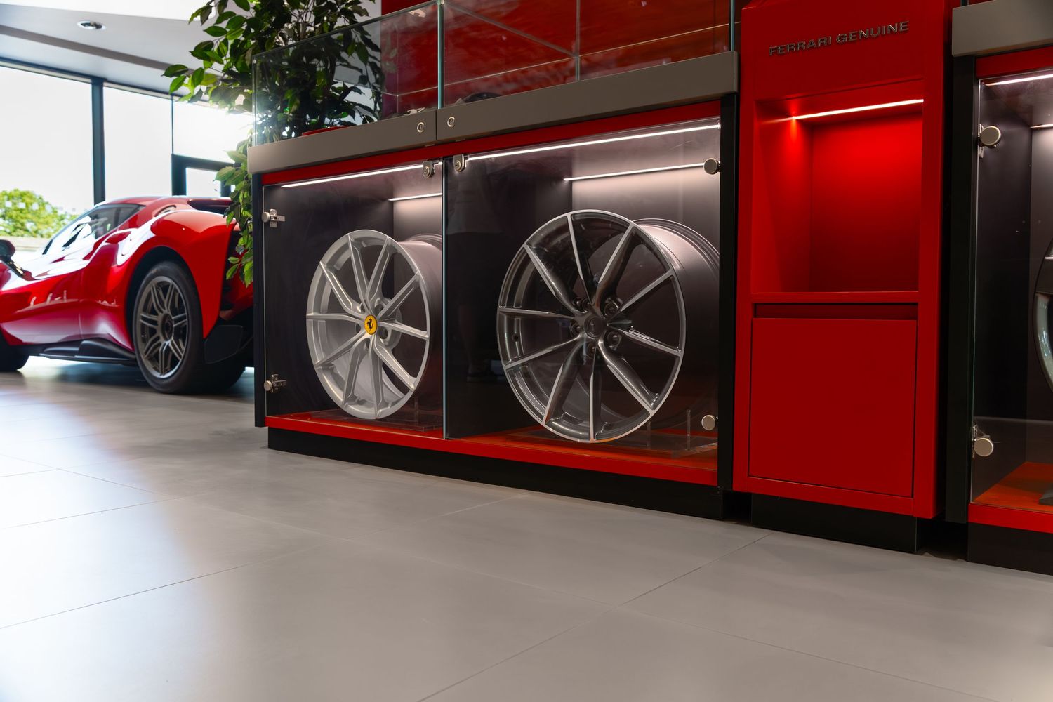 Ferrari dealership showroom displaying luxury alloy wheels in illuminated red display cabinets with a red Ferrari visible in background.