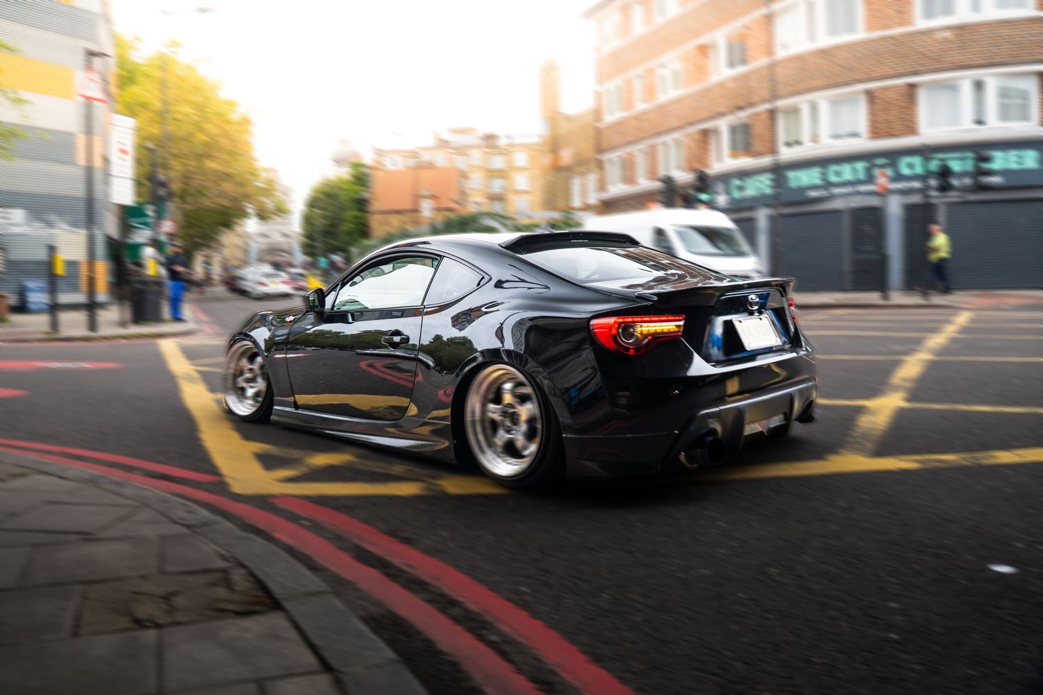 Dark blue modified Toyota GT86 with wide body kit driving through London streets at dusk.