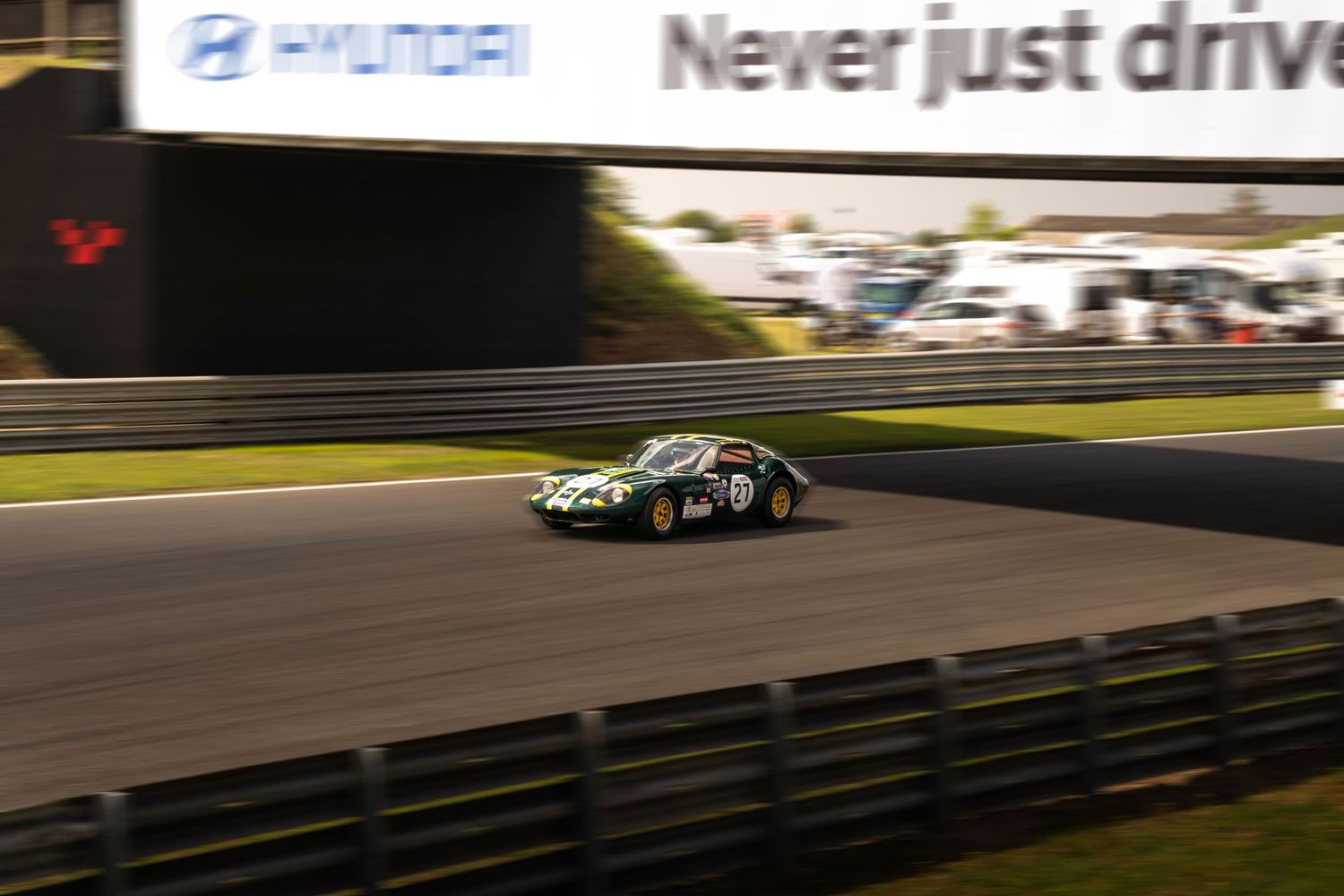 Vintage green racing car competing on track at dusk under Hyundai Never Just Drive banner.