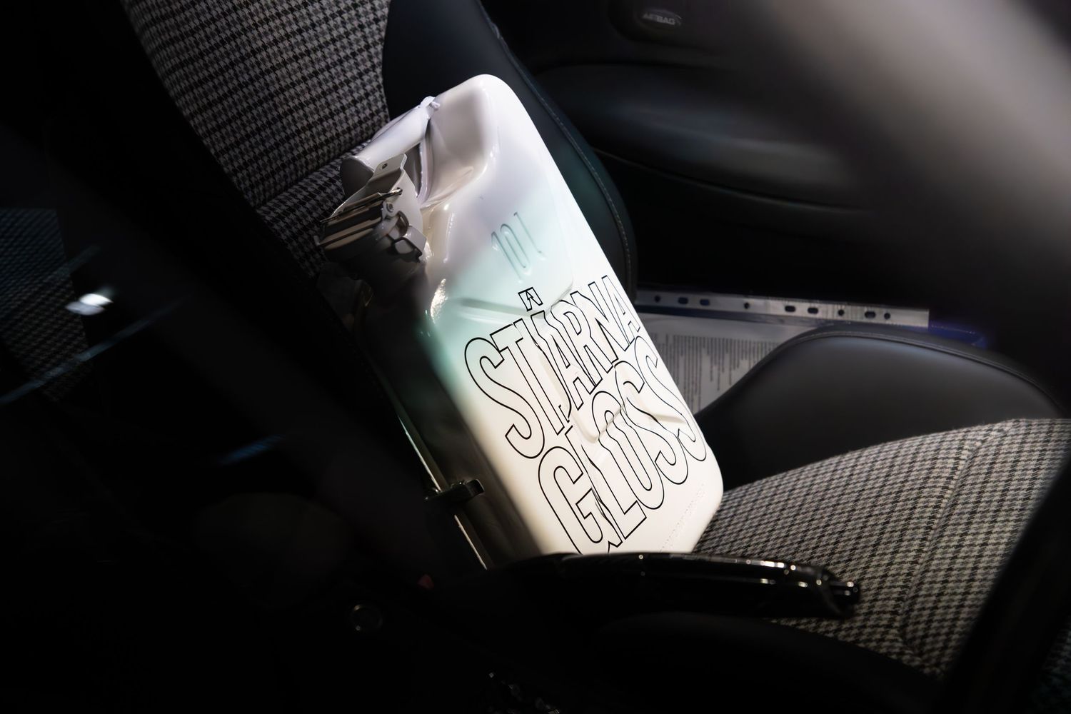 A bottle of Star Gloss car detailing product resting on a car seat interior.