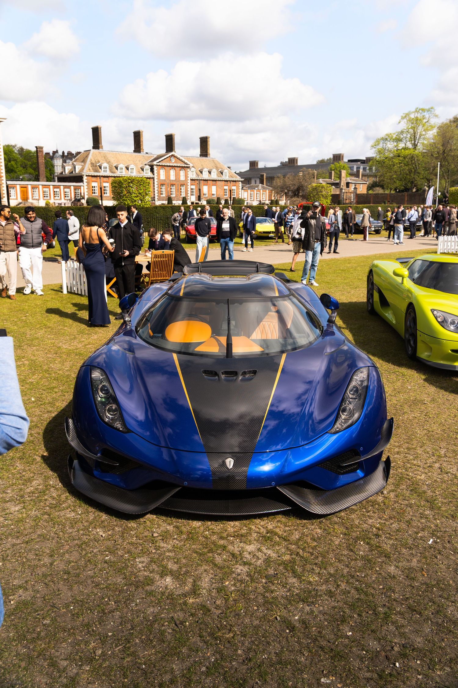 Blue Koenigsegg Regera hypercar on display at an outdoor car show with historic building backdrop.