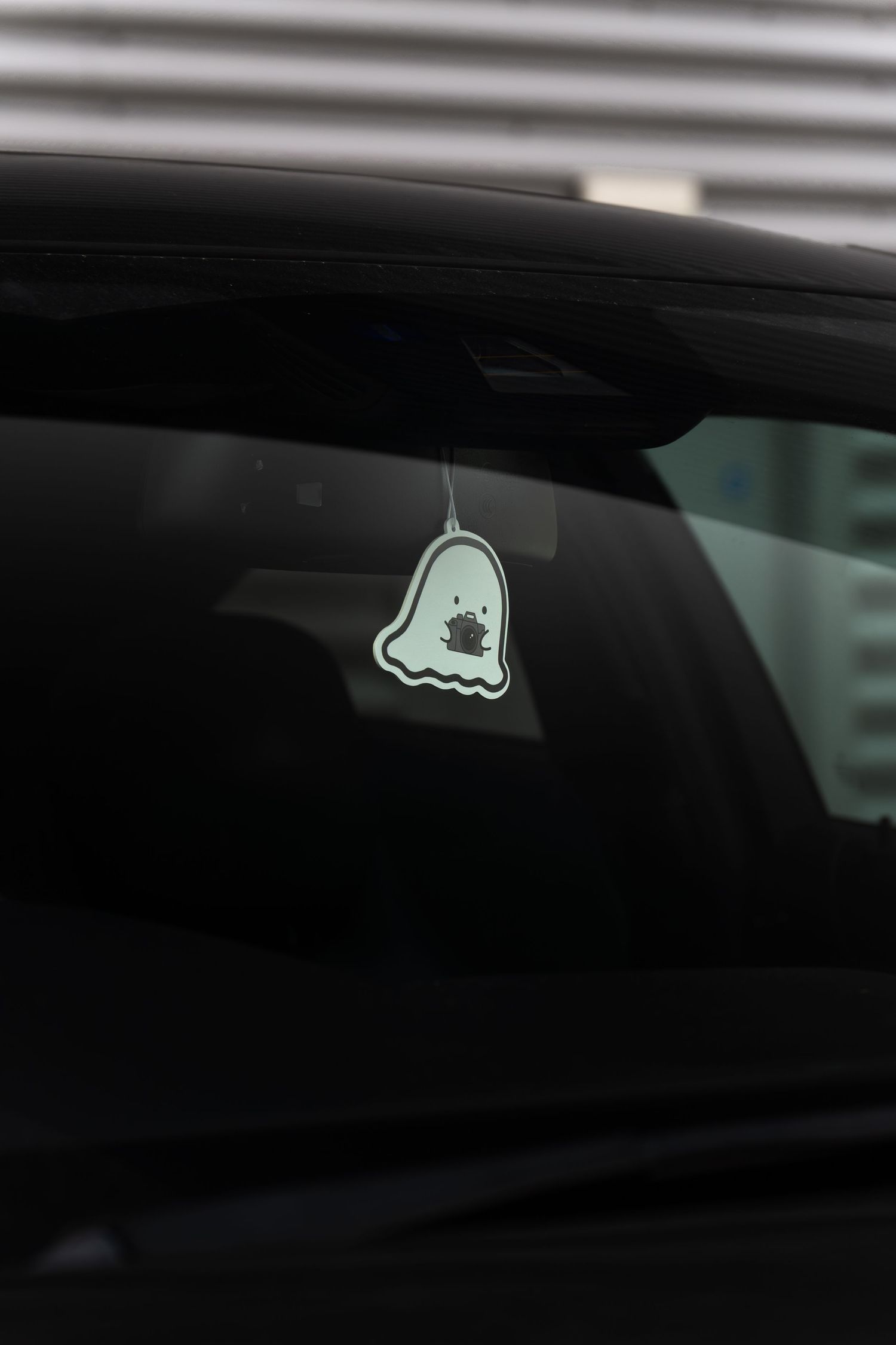 Ghost-shaped air freshener hanging from rearview mirror inside black Mercedes-AMG C63 coupe.