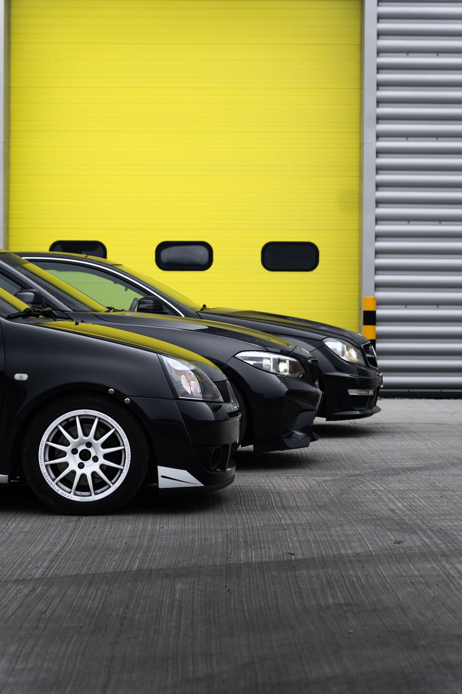 Close-up of two black performance cars with yellow accents parked in front of a yellow garage door.
