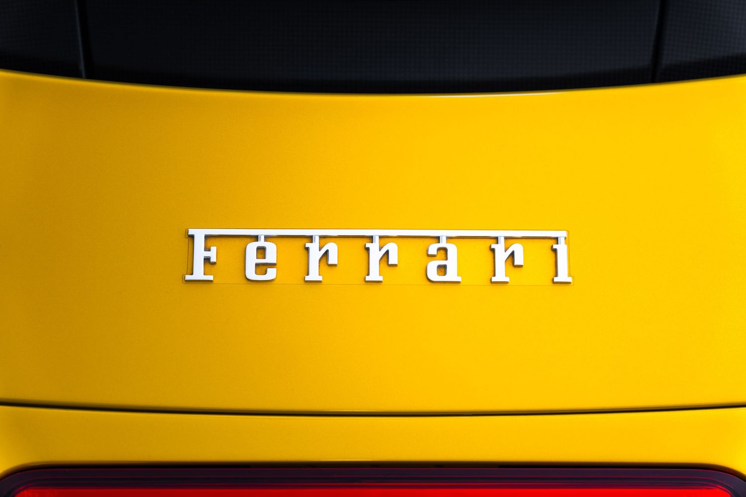 Close-up of a chrome Ferrari logo badge on a vibrant yellow car exterior.