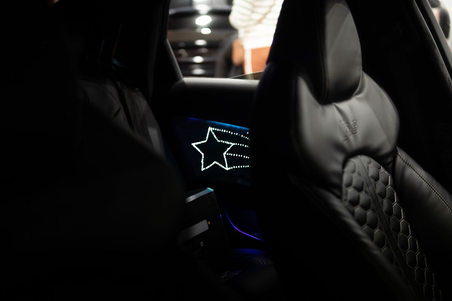 Dark luxury car interior featuring an illuminated star design on quilted leather rear seat.