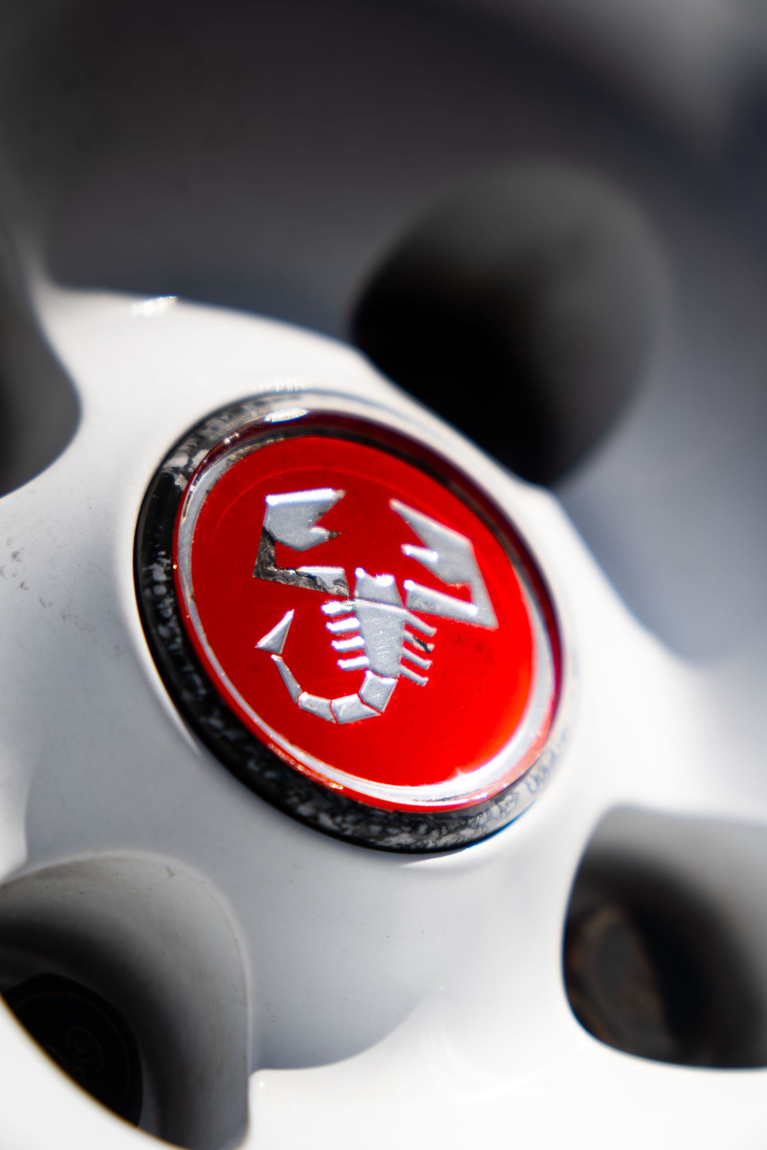 Close-up of an Abarth scorpion logo on a red centre cap of a white alloy wheel.
