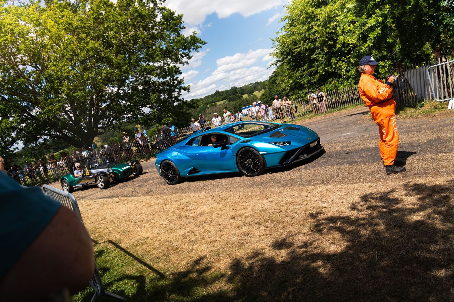 A vibrant blue Lamborghini Huracan drives past marshals and spectators at the Goodwood Festival of Speed hillclimb event.