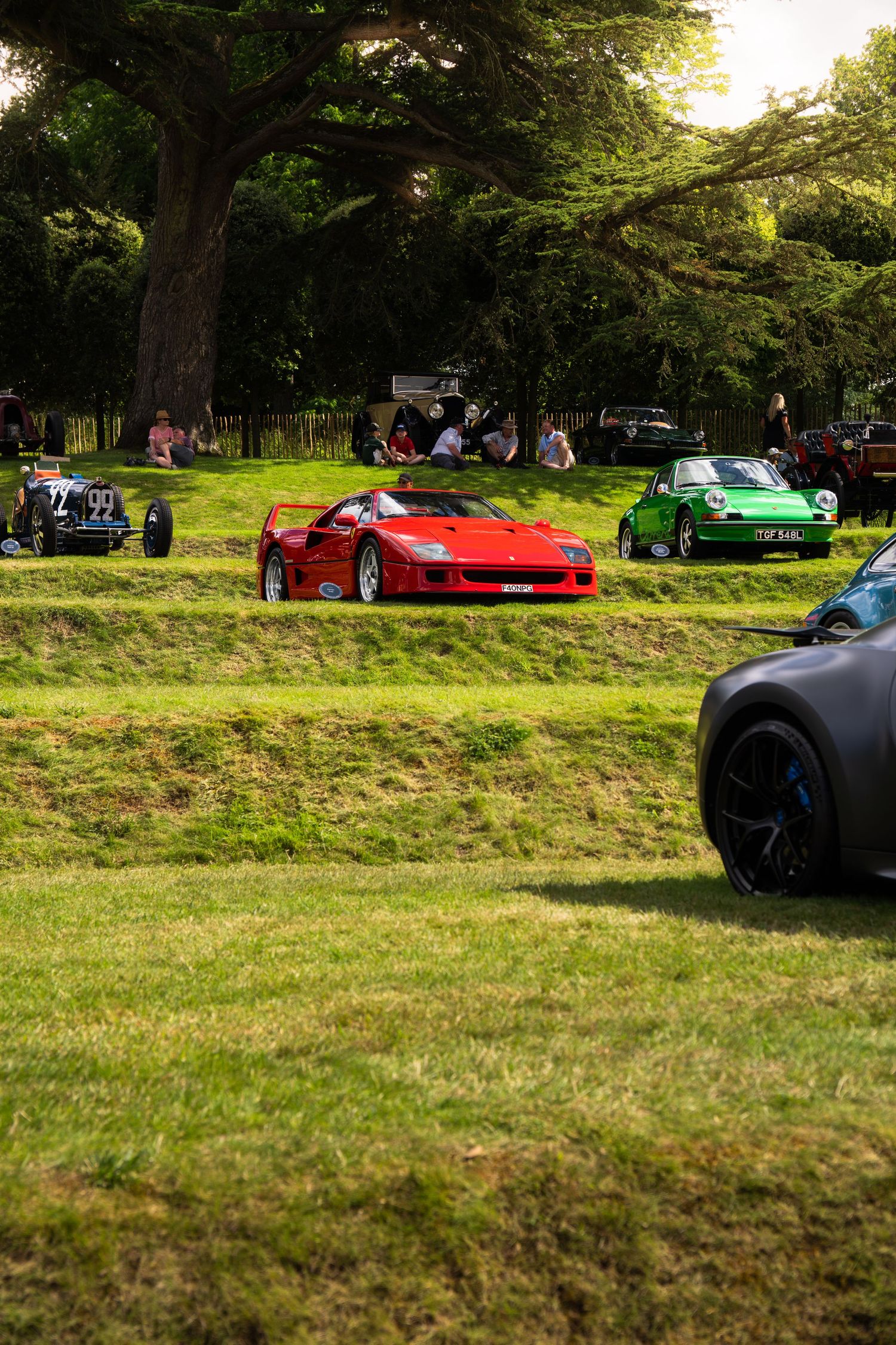 Red Ferrari F40 and green Porsche on display at an outdoor classic car show on a lush green lawn.