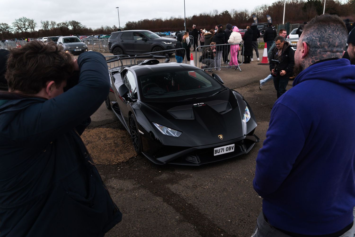 Matte black Lamborghini Huracan being photographed by enthusiasts at an outdoor car meet.