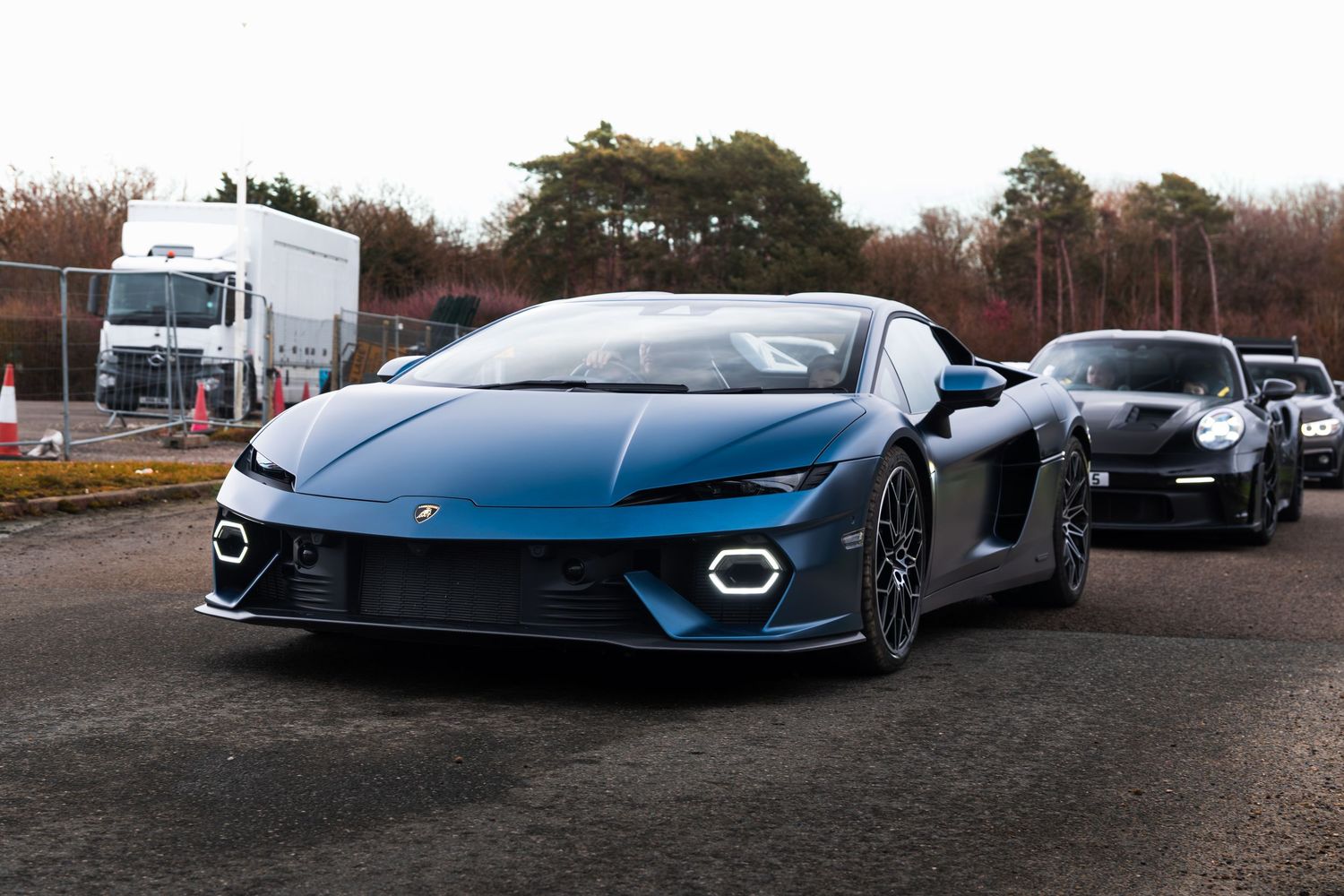 A blue Lamborghini Huracan Tecnica supercar leads a lineup of exotic cars at an outdoor meet.