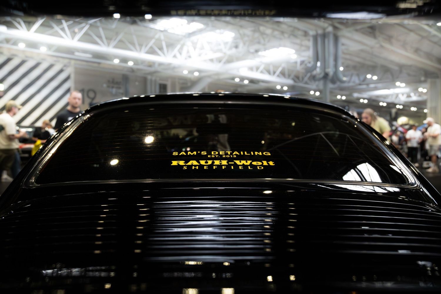 Rear view of a black car displaying Sam's Detailing and Raywell sponsor decals at a car show.