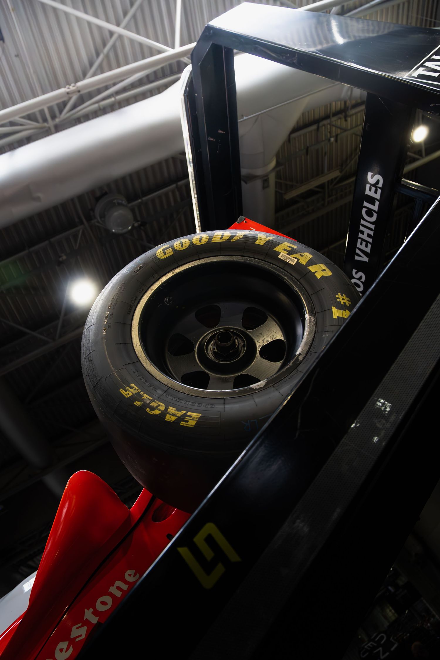 A Goodyear Eagle tire on a black and red Formula racing car displayed in an indoor exhibition.