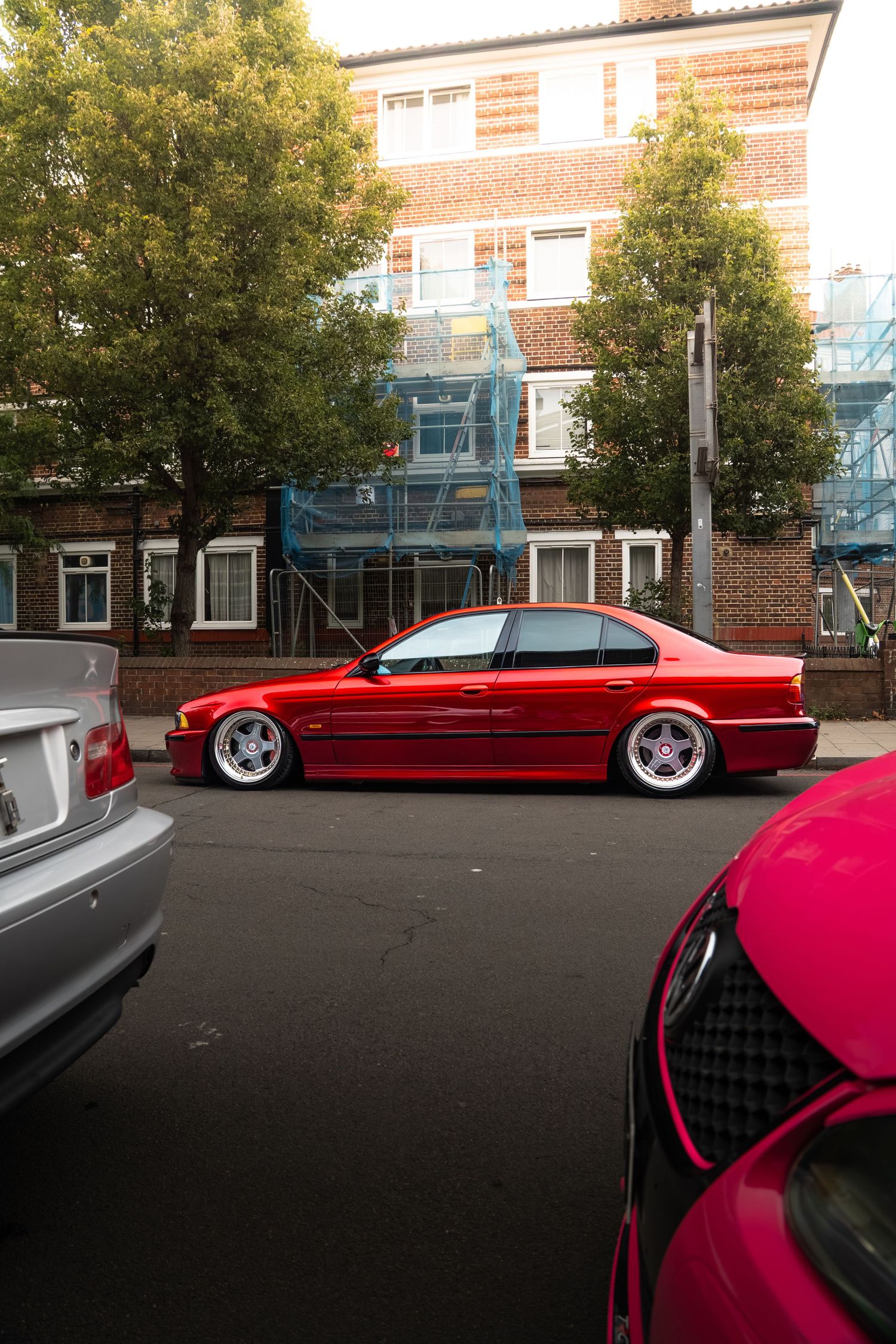 A lowered red BMW E38 7-Series on white BBS wheels parked on a street outside a brick building.