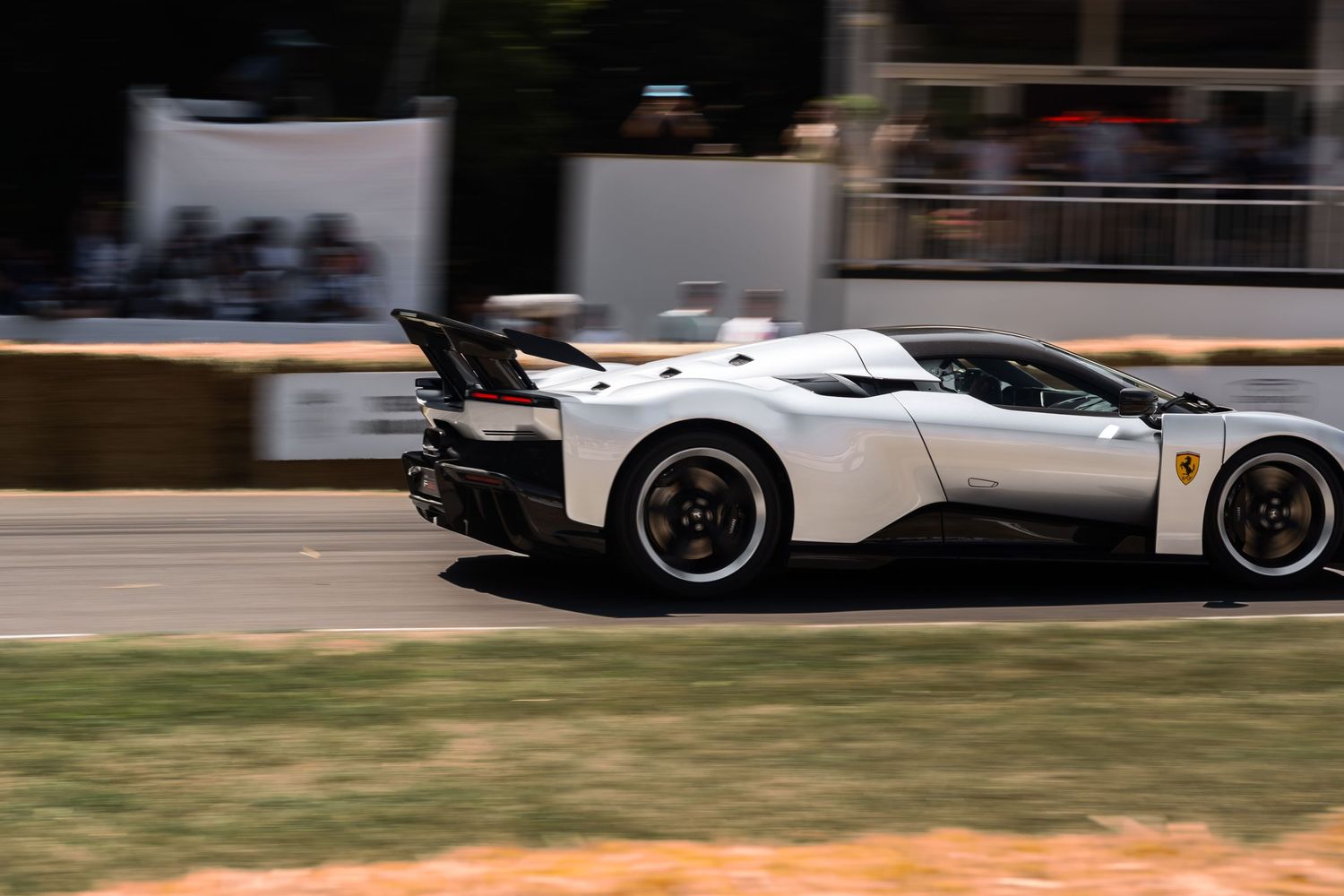 White Ferrari hypercar speeding past spectators at the Goodwood Festival of Speed hillclimb event.