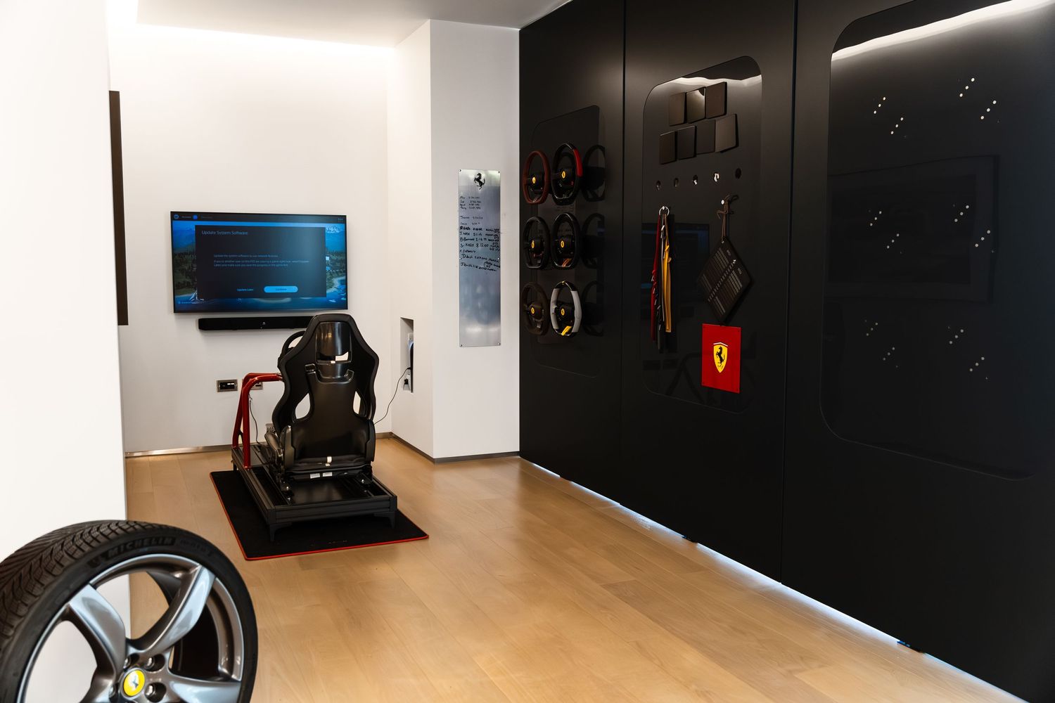 Ferrari-themed showroom with racing seat simulator, branded accessories wall, tire display, and flat-screen monitor on white wall.