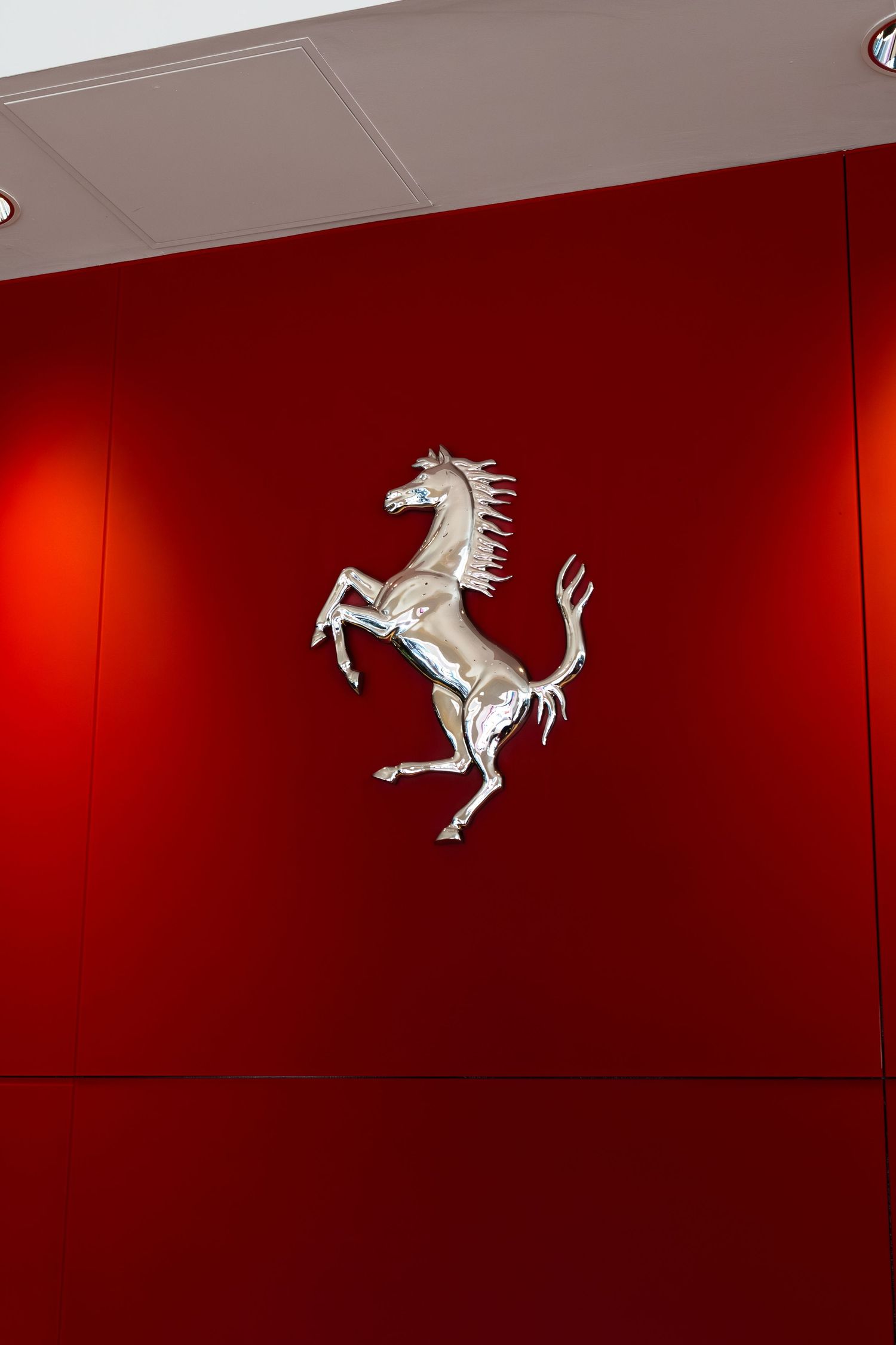 Silver Ferrari prancing horse logo mounted on a vibrant red wall in a Ferrari dealership.