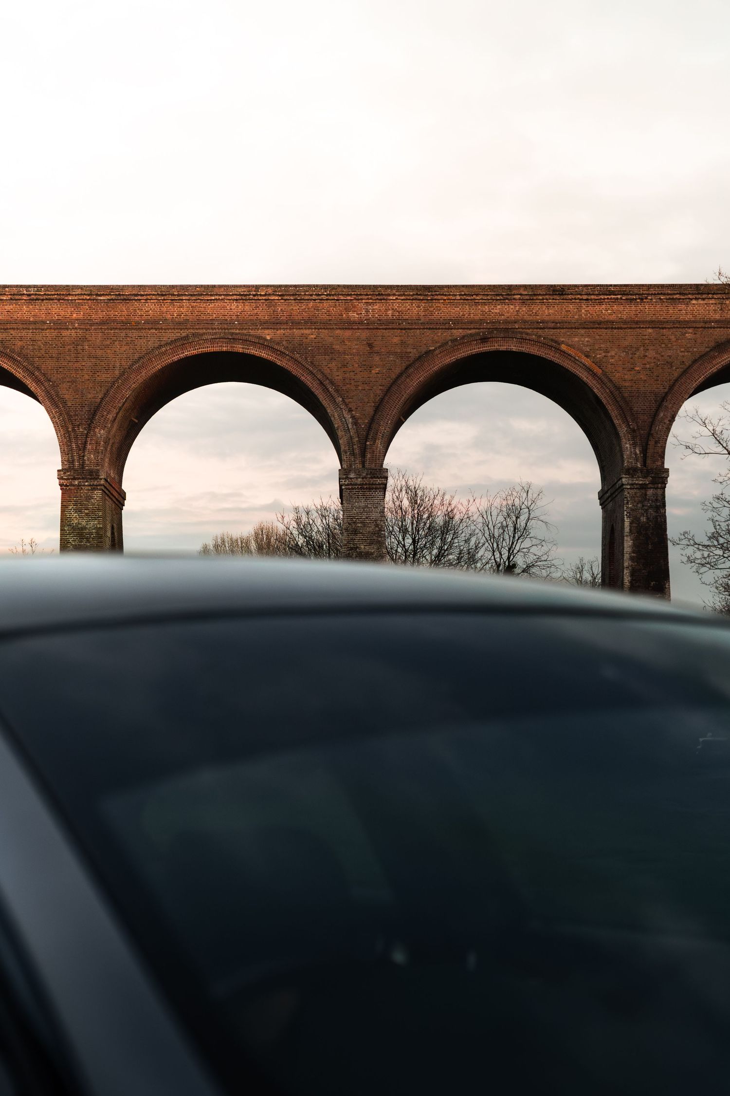 Brick railway viaduct with arched spans framed above blurred BMW M3 roofline.