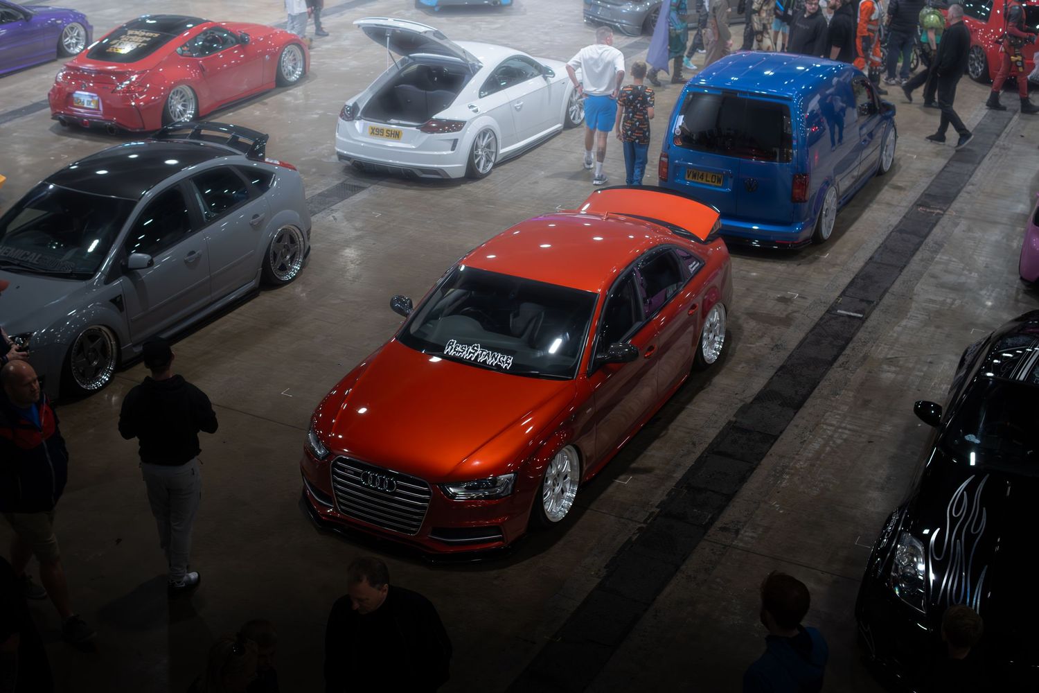 Aerial view of modified cars including an orange Audi at an indoor automotive exhibition.
