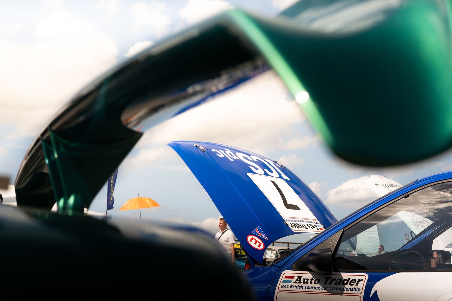 Blue AutoTrader racing car with open hood at a motorsport event under dramatic sky.