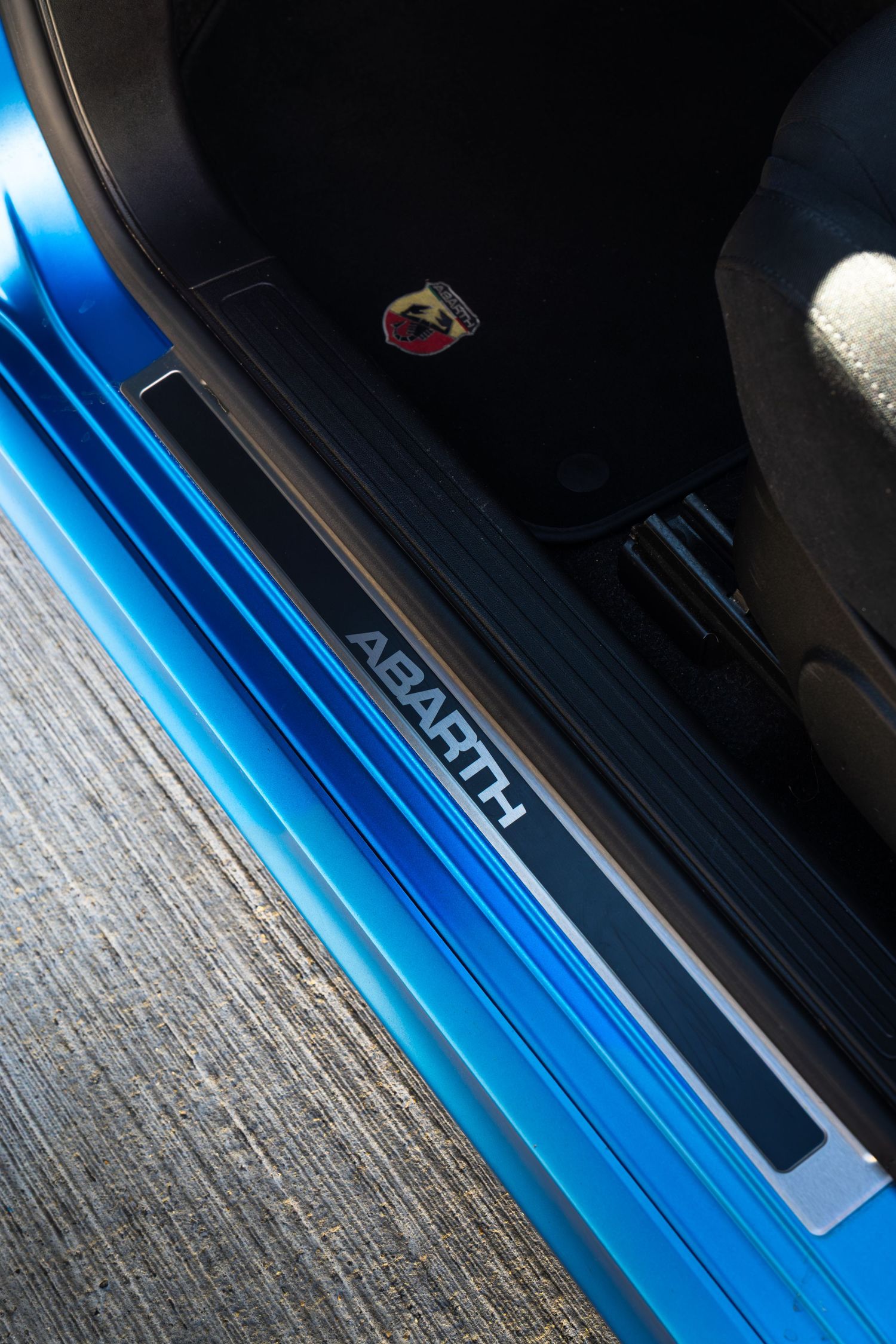 Close-up of an Abarth door sill plate in blue with the Abarth scorpion logo badge visible above.