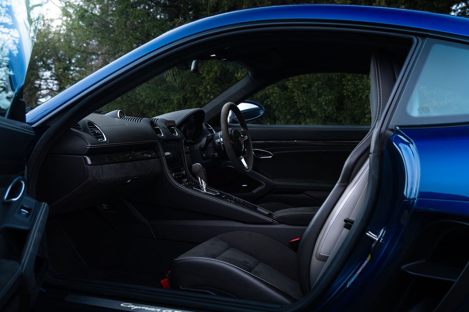 Interior side view of Porsche 718 Cayman GTS showing black sport seats, dashboard and open door.