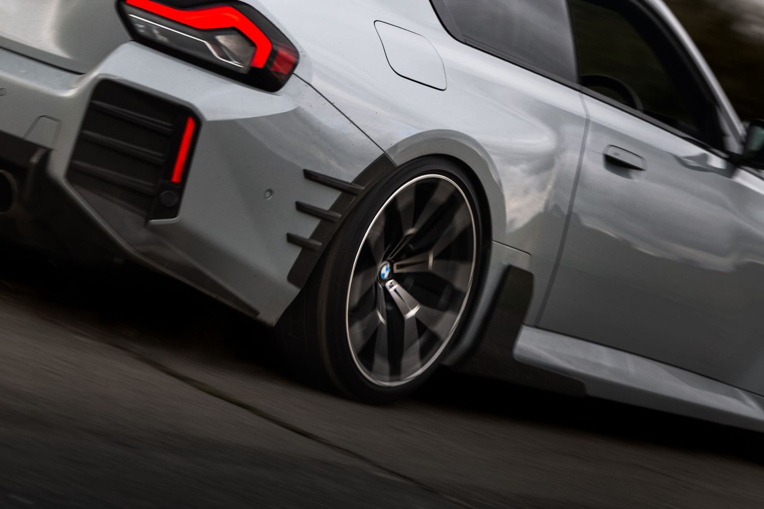 Close-up of a lowered white BMW M2 rear quarter panel featuring dark alloy wheels and red brake calipers.