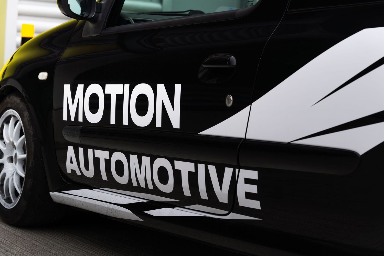 Close-up of Motion Automotive white vinyl lettering on the door of a black Renault Clio.