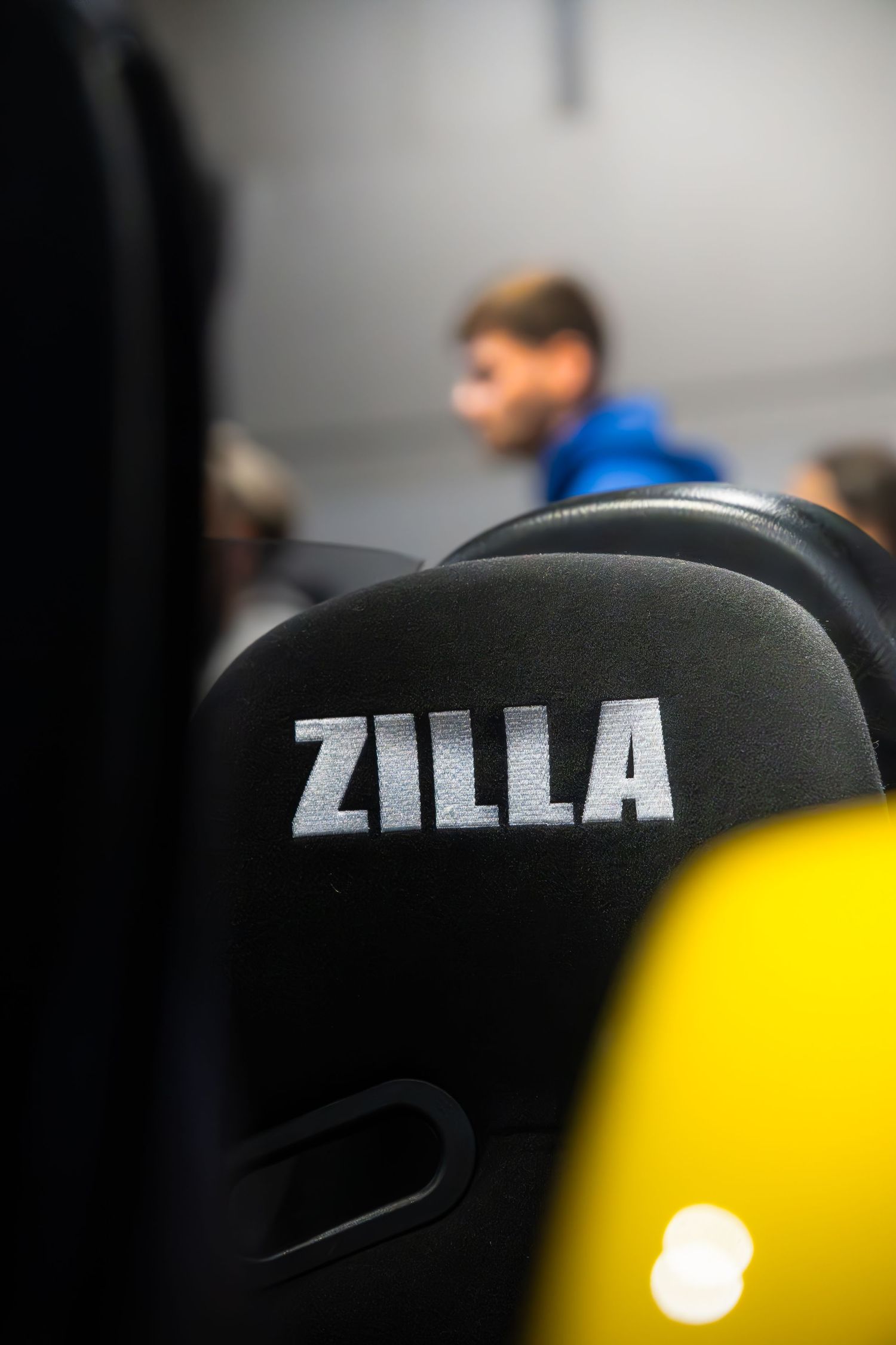 Close-up of a black racing seat with ZILLA embroidered in white letters at a car show.