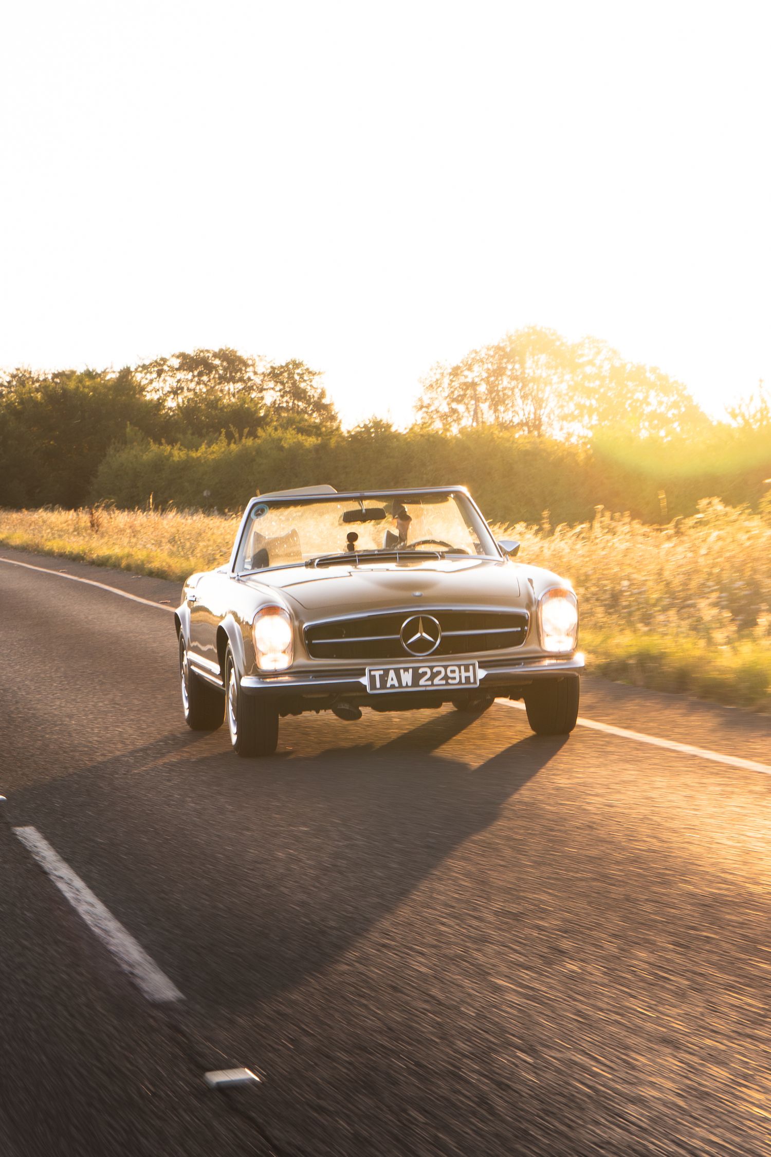 Vintage Mercedes-Benz convertible driving on a scenic road at golden sunset hour.