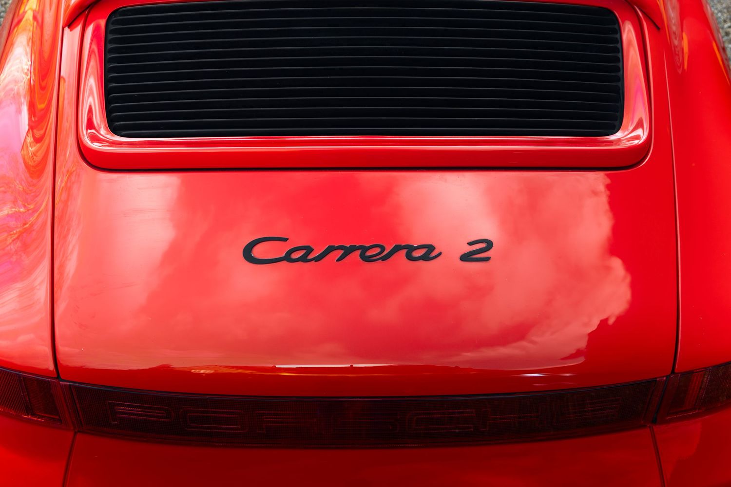 Close-up of the red Porsche 911 rear engine lid showing the Carrera 2 script badge in black lettering.