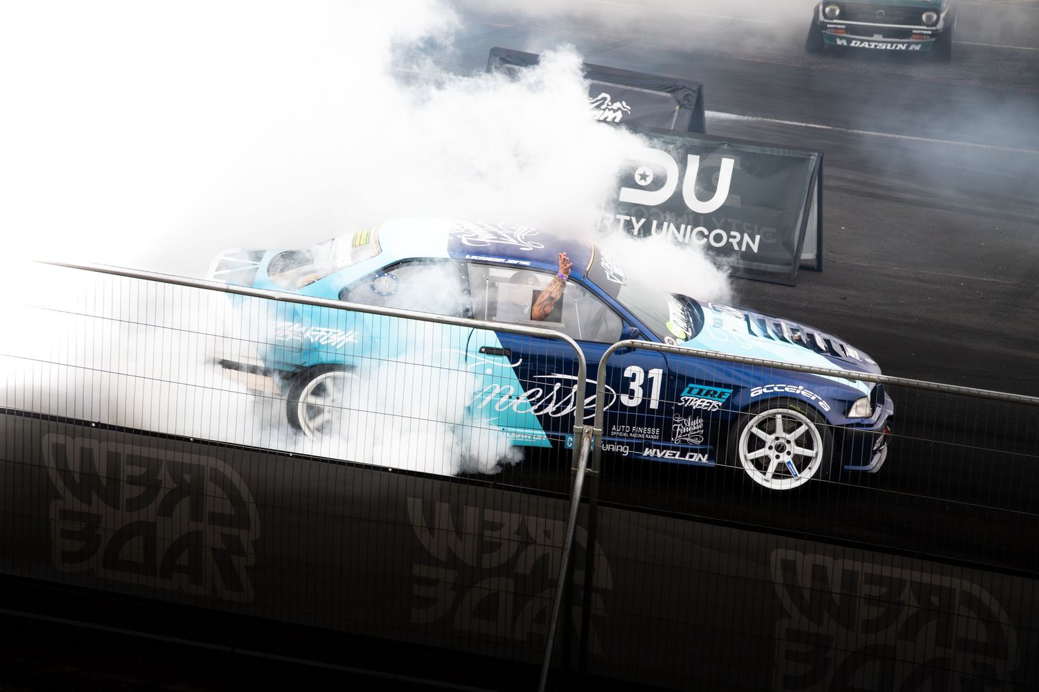 A blue BMW number 31 drift car spins surrounded by thick white smoke at an indoor motorsport event.