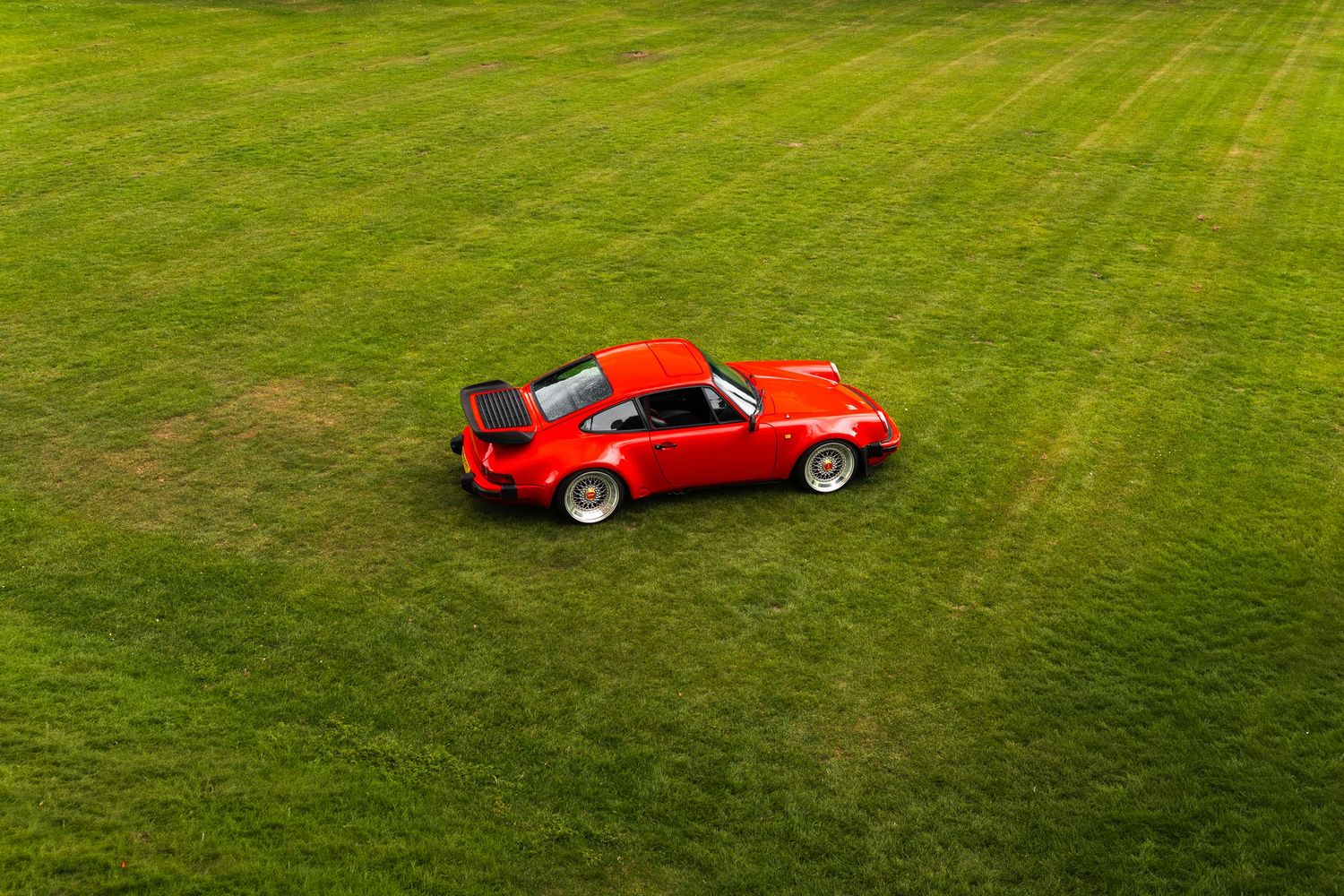Red Porsche 911 sports car parked on lush green grass, aerial view showcasing classic design and rear spoiler.
