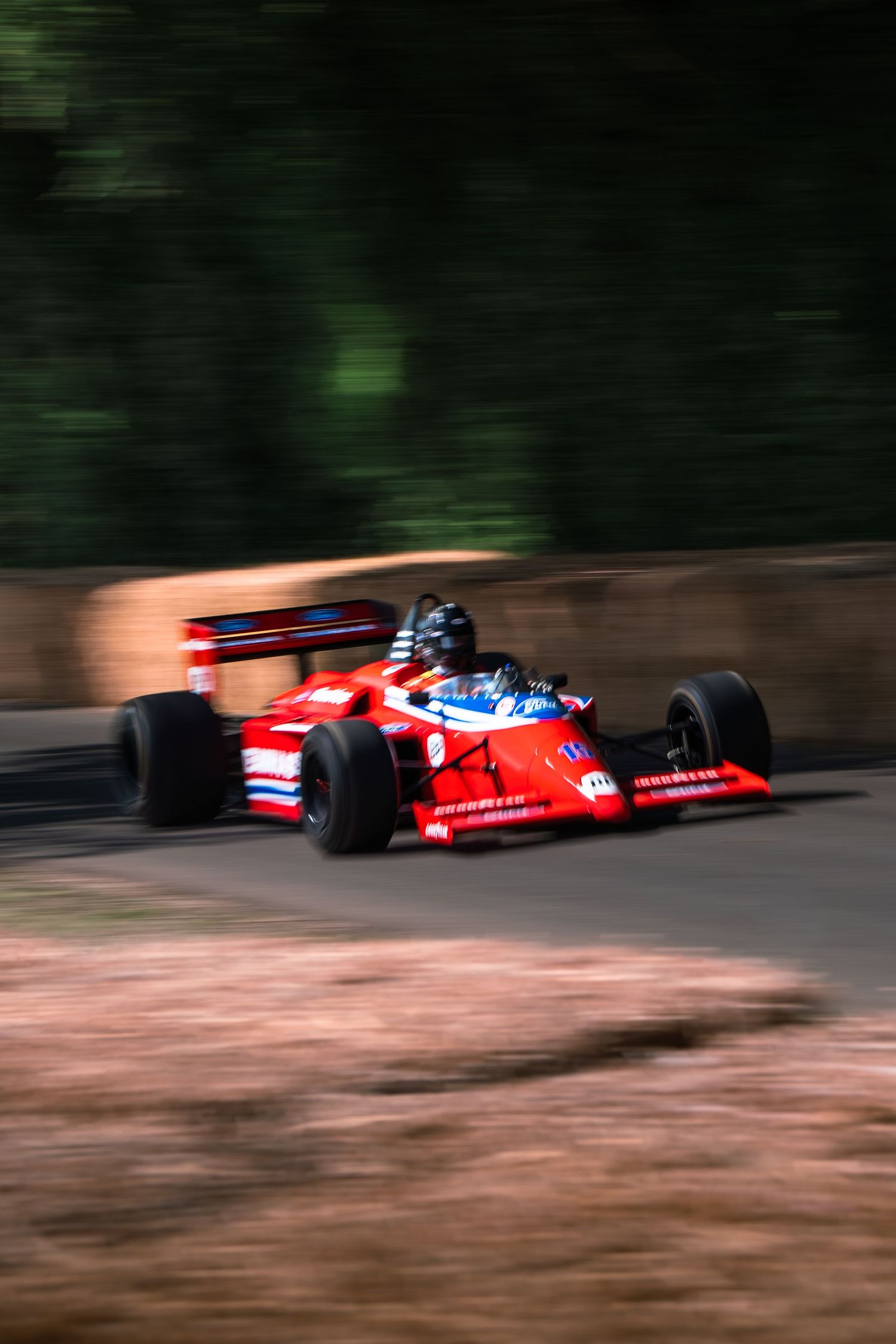 Red Formula 1 racing car speeding on a track, motion blur background, driver in helmet, classic open-wheel race car.
