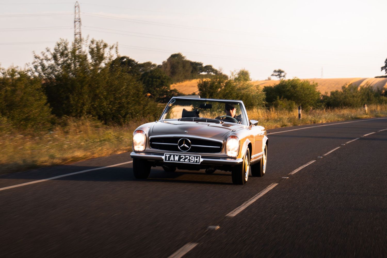 Classic Mercedes-Benz convertible cruising on a rural road at golden hour sunset.