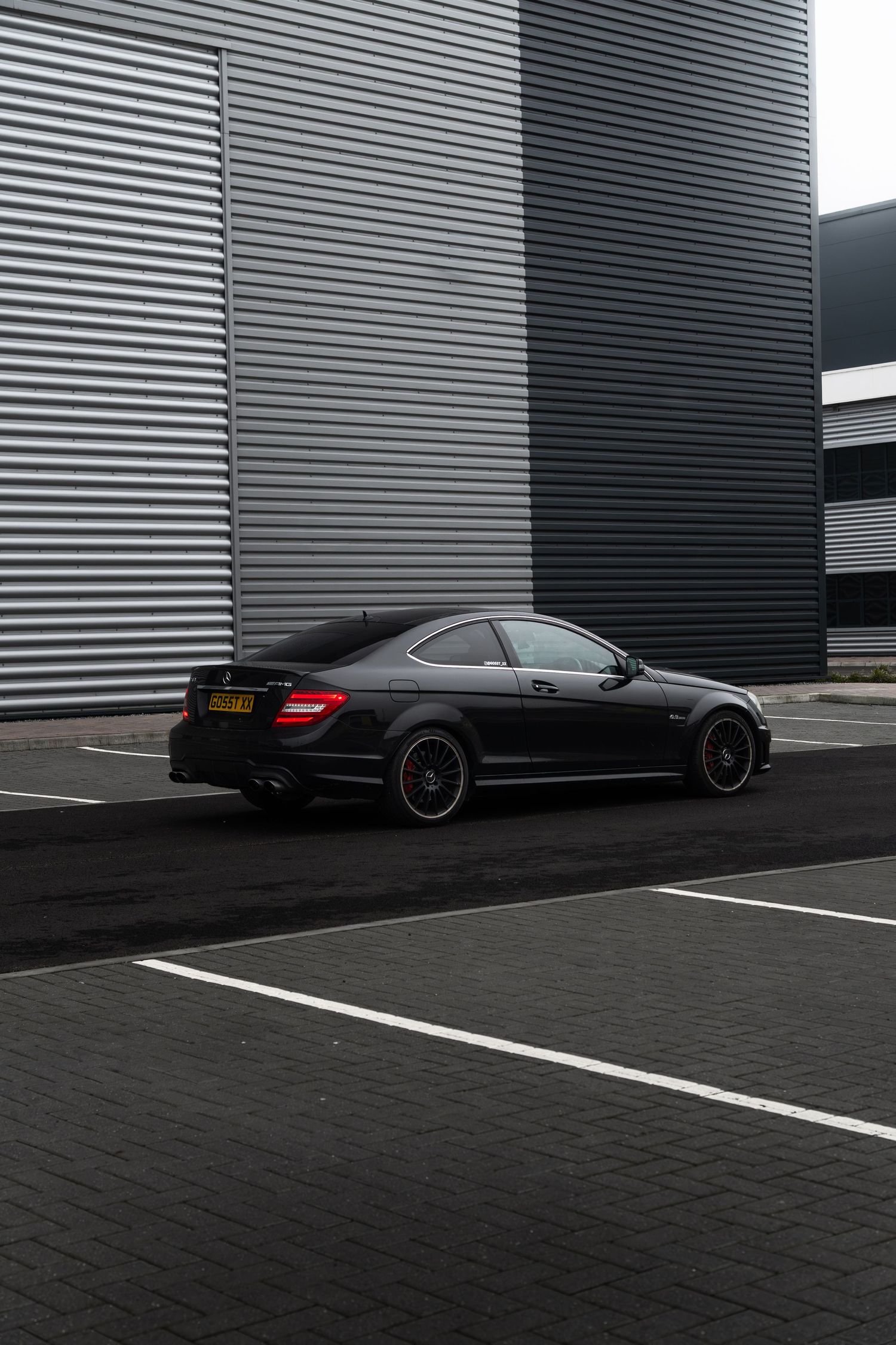 Black Mercedes-AMG C63 coupe photographed from rear three-quarter angle at an industrial location.