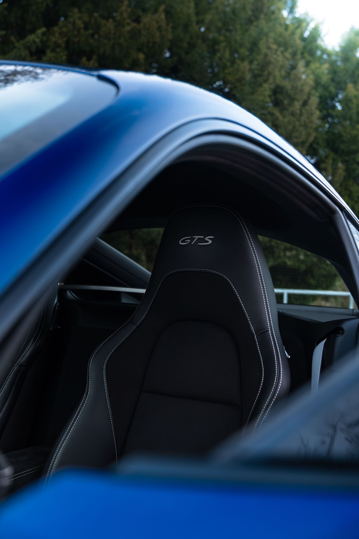 Interior view through window of Porsche 718 Cayman GTS showing black GTS-embroidered sport seat.