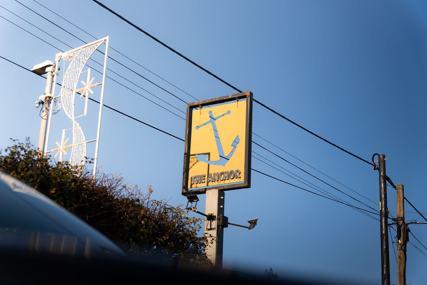 Yellow The Anchor pub sign against a clear blue sky with decorative star light display.
