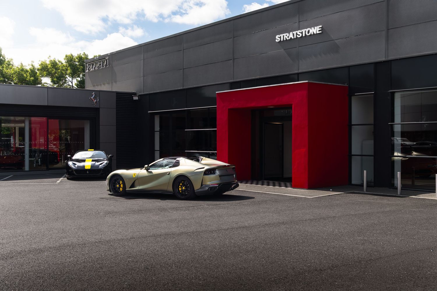 Stratstone Ferrari dealership exterior with silver and yellow supercars parked outside a modern black building.