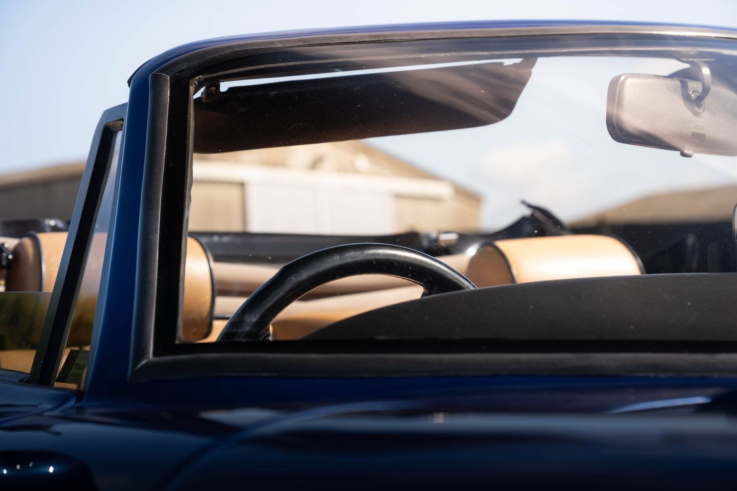 Interior view through windscreen of a classic dark blue convertible car showing steering wheel.