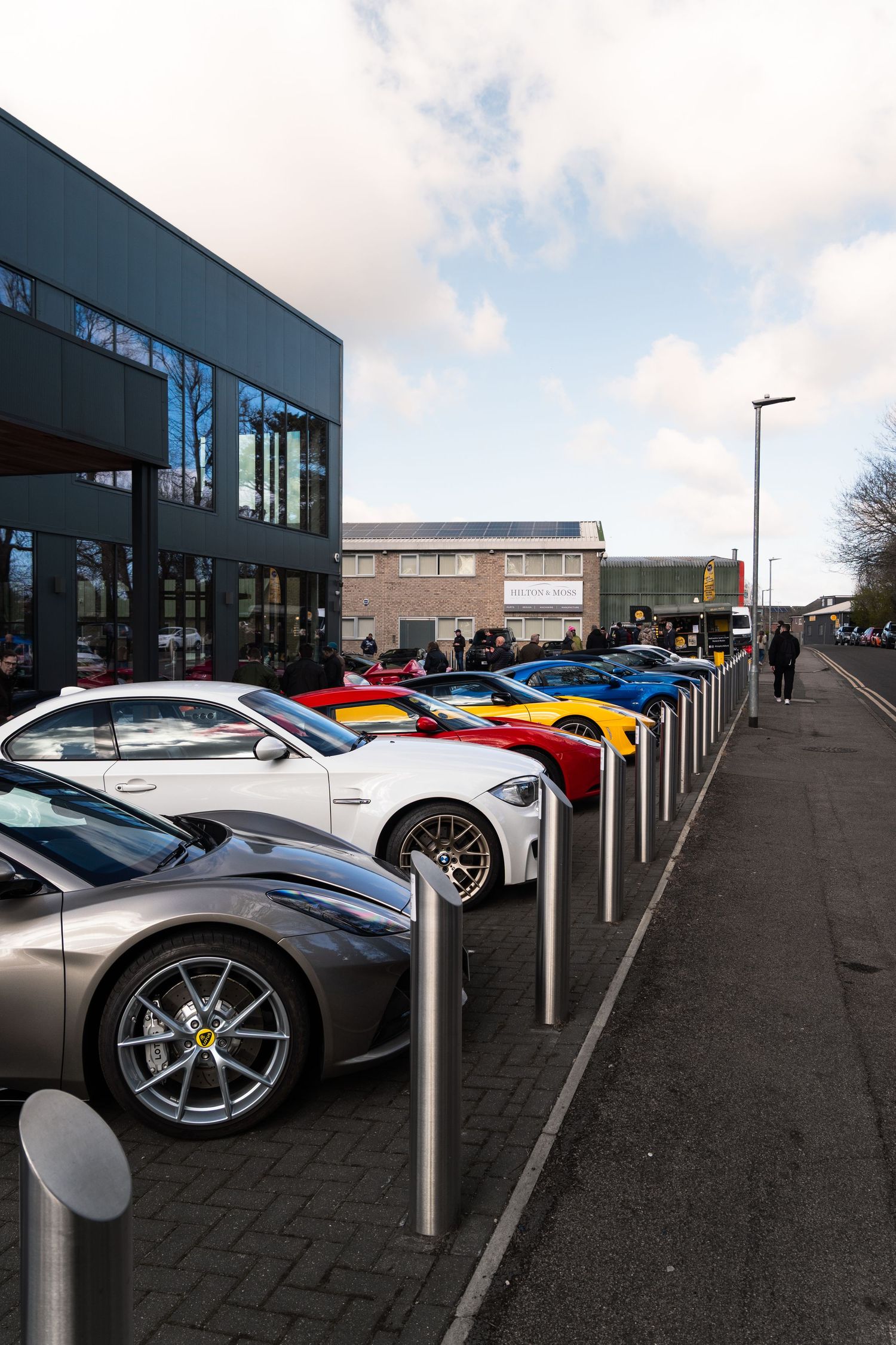 Row of colorful exotic sports cars parked outside modern dealership building.