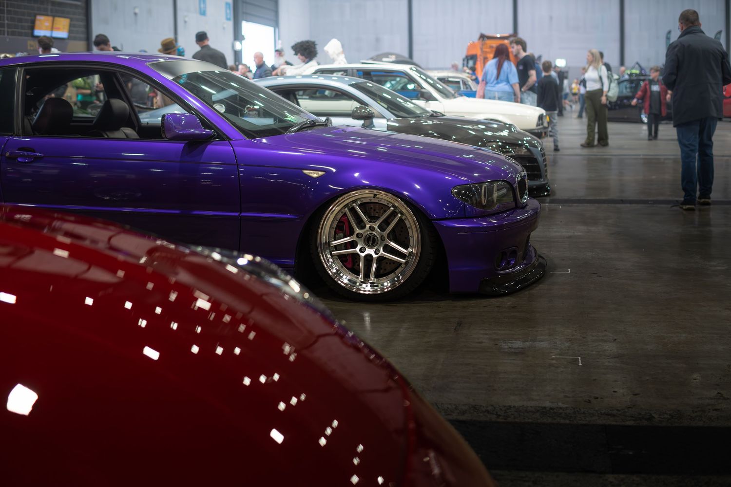 A slammed purple BMW E46 with chrome mesh wheels on display at an indoor car show.