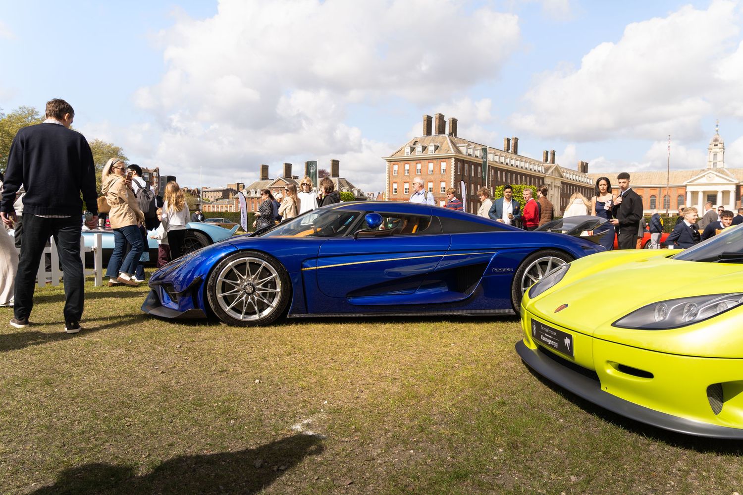 Blue Koenigsegg Regera hypercar displayed at an outdoor automotive show near a historic building.