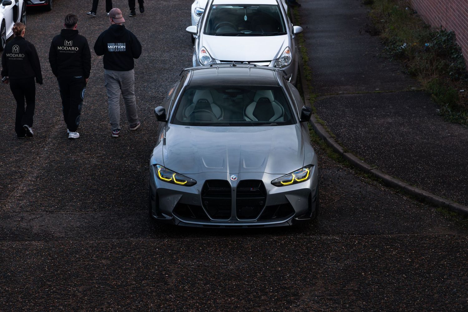 Aerial view of a silver BMW M3 G80 with yellow angel eyes at a car meet.